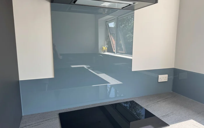 Modern kitchen with a glossy blue Glass splashback, gray countertop, and an open window reflecting outside scenery.